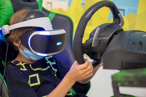 Το παιδί από την Ευρώπη παίζει παιχνίδια εικονικής πραγματικότητας φορώντας γυαλιά εικονικής πραγματικότητας και εξερευνήστε την εναλλακτική πραγματικότητα. Cyber χώρος και εικονικό gaming, Παίζοντας με joystick βιντεοπαιχνίδια. - Φωτογραφία, εικόνα