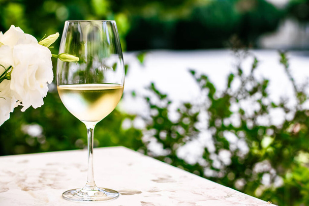 夏の庭のテラスでの高級レストランでの白ワイン、ブドウ畑でのワイナリーでのワインテイスティング、グルメツアーや休暇旅行 - 写真・画像
