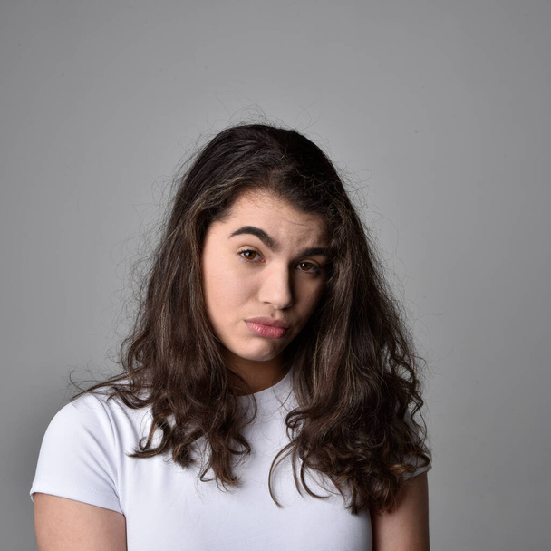 Primer plano retrato de mujer joven con cabello castaño natural, sobre las expresiones faciales superiores sobre fondo de estudio gris claro. - Foto, Imagen