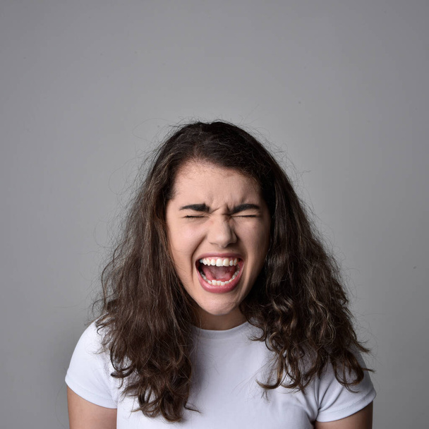 Close up retrato de jovem mulher com cabelo castanho natural, sobre as expressões faciais superiores em fundo estúdio cinza claro. - Foto, Imagem