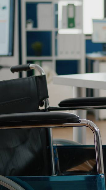Wózek inwalidzki zaparkowany w pustym pomieszczeniu biurowym przy biurku w firmie start-up - Zdjęcie, obraz