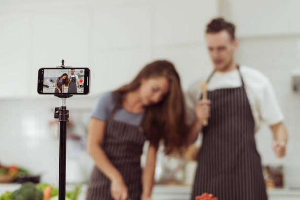 Концепція Блогер і Youtuber, Щаслива пара любить записувати відео під час приготування їжі разом на кухні. Фокус на смартфоні, пара готує разом на прямому ефірі
. - Фото, зображення