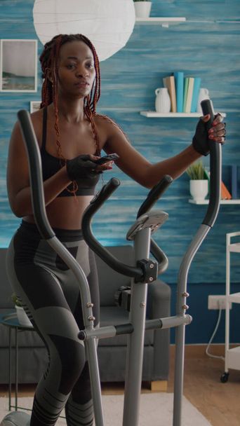 Велосипедистка с черной кожей в спортивной одежде тренирует мышцы тела с помощью эллиптических - Фото, изображение