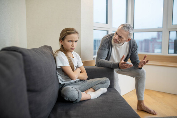 Gray-haired bearded man talking to his kid while she looking moody - Foto, immagini