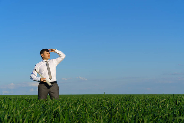 επιχειρηματίας θέτει με ένα spyglass, κοιτάζει στην απόσταση και ψάχνει για κάτι, πράσινο γρασίδι και μπλε ουρανό ως φόντο - Φωτογραφία, εικόνα