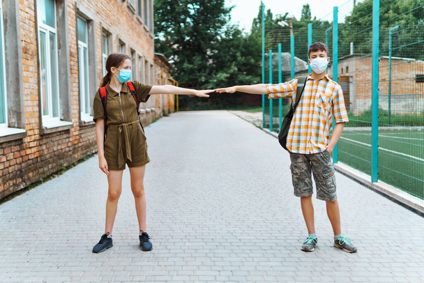 két tinédzser fiú és lány útban az iskola felé, védőmaszkot használnak és társadalmi távolságot mutatnak a koronavírus fertőzés ellen. - Fotó, kép
