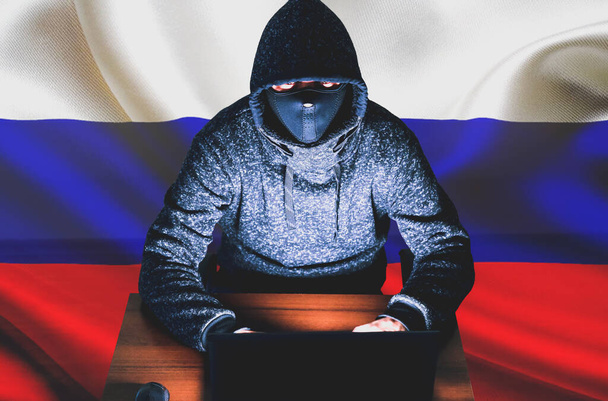 Ο άντρας με κουκούλα χακάρει προσωπικά δεδομένα. Ασφάλεια πληροφοριών με ρωσική σημαία. Προστασία της έννοιας της ενημέρωσης. Κακό κωδικό πρόσβασης. - Φωτογραφία, εικόνα