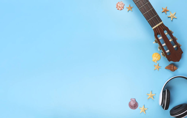 青い背景に貝殻やヒトデとヘッドフォンやアコースティックギターのトップビューや背景、コピースペース。夏のビーチアコースティック音楽の背景. - 写真・画像