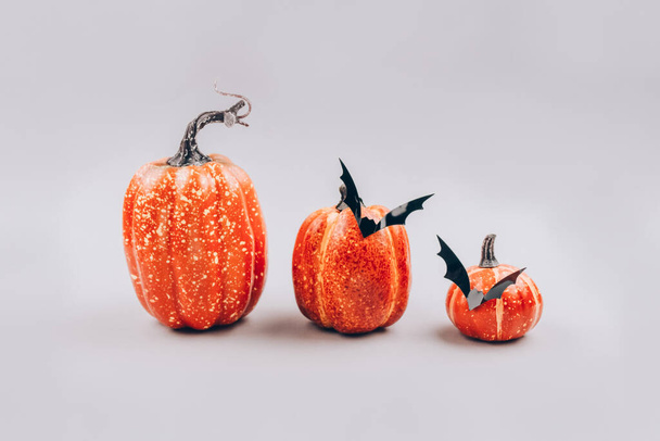 Mínimo Halloween assustador e conceito. Abóboras laranja decorativas com morcegos no fundo cinza claro com espaço de cópia. Decorações de Halloween ou convite de festa. Foco seletivo - Foto, Imagem