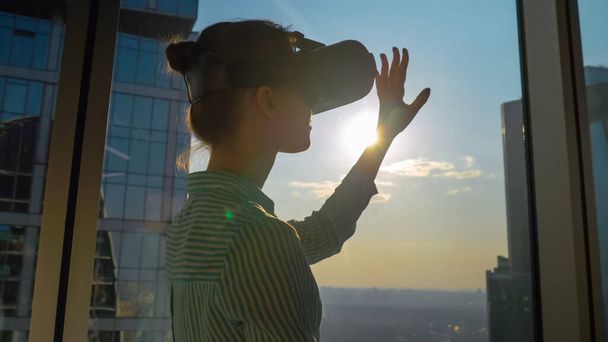 VR concept - giovane donna che utilizza cuffie di realtà virtuale contro la finestra del grattacielo - Foto, immagini