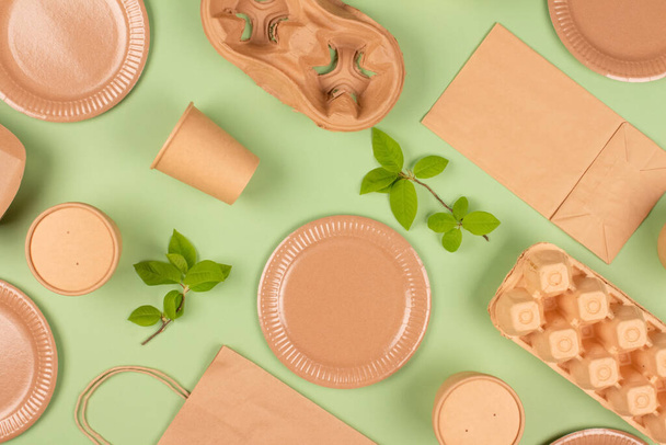 Flat lay composition with eco-friendly tableware and kraft paper food packaging on green background. Sustainable packaging, recyclable paperware, zero waste packaging concept. Selective focus, mockup - Photo, image