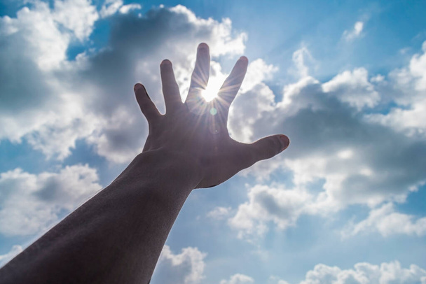 рука в бік сонячного неба в яскравому денному світлі. сонячні промені з проміжку пальців
 - Фото, зображення