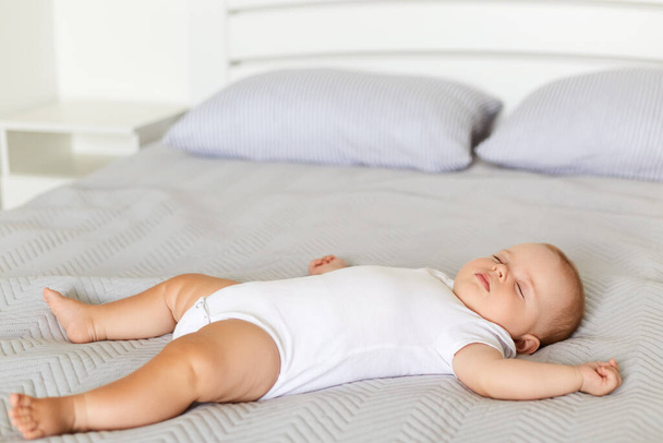 Peaceful baby lying on a bed while sleeping in a soft bed on grey blanket, infant wearing white bodysuit sleeps alone indoor, childhood. - Foto, Imagen