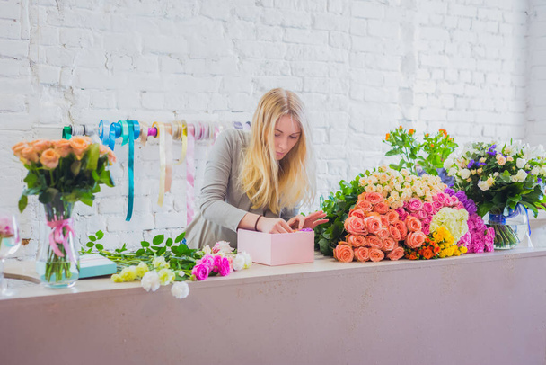 Női virágművész, virágárus ajándékdobozt készít virágokkal az asztalon - Fotó, kép