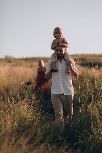 Young parents with son and husky dog walking in summer field. Family time, have fun. - Fotó, kép