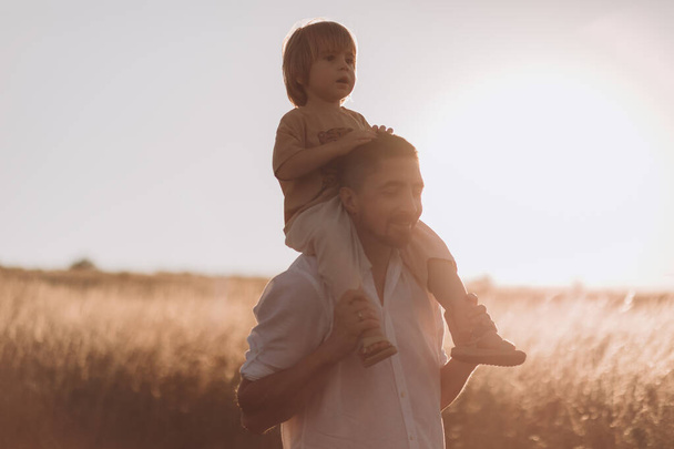 Το μικρό αγόρι παίζει με τον μπαμπά το καλοκαίρι στο ηλιοβασίλεμα στο χωράφι.  - Φωτογραφία, εικόνα