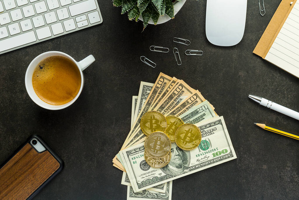 Flat lay top view office desk working space with keyboard and smartphone, watch, plant, coffee, usd dollars and bitcoin on black background - 写真・画像