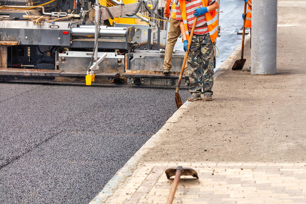 Um paver industrial está colocando uma camada de novo asfalto quente na pista. O trabalhador controla a uniformidade da pavimentação com uma pá. Espaço de cópia. - Foto, Imagem