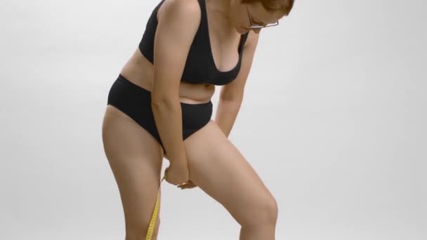 Plus size giovane donna caucasica misurare la gamba. Studio di sfondo bianco video di alta qualità. - Filmati, video