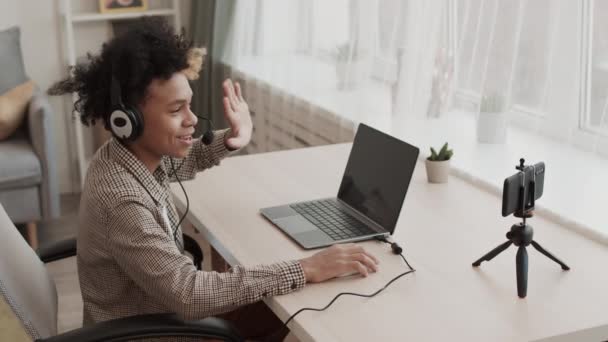 Vysoký úhel kudrnatého dospívajícího chlapce ve sluchátkách s mikrofonem, sedí za stolem ve svém pokoji, hraje videohru na přenosném počítači ve dne - Záběry, video