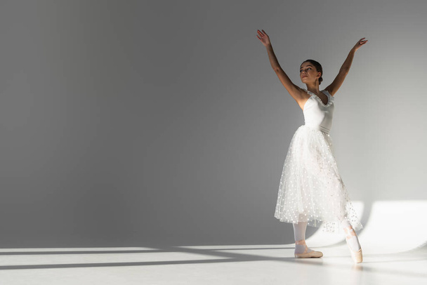 Young ballerina in white dress dancing on grey background  - Photo, Image