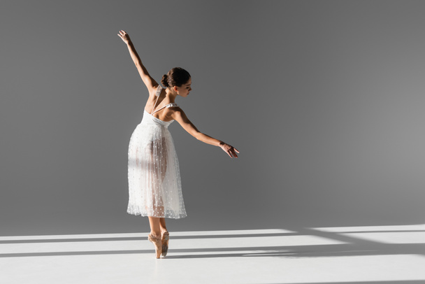 Side view of elegant ballerina in pointe shoes on grey background with sunlight - Fotó, kép