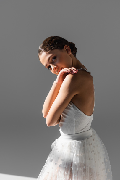 Pretty ballerina looking at camera on grey background with sunlight - Foto, immagini