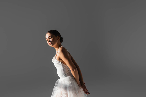 Young ballerina standing in sunlight isolated on grey  - Foto, imagen
