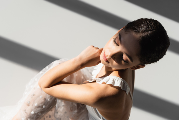 Overhead view of pretty ballerina sitting on grey background with sunlight and shadow  - Foto, Imagem