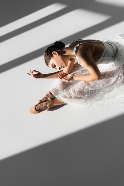 Korkea kulma näkymä ballerina suljettu silmä tanssia lattialla harmaalla pohjalla auringonvalolla - Valokuva, kuva
