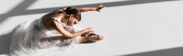 High angle view of ballerina in pointe shoes bending on grey background with sunlight, banner  - Zdjęcie, obraz