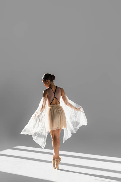 Side view of ballerina in pointe shoes dancing with cloth in sunlight on grey background  - Foto, imagen