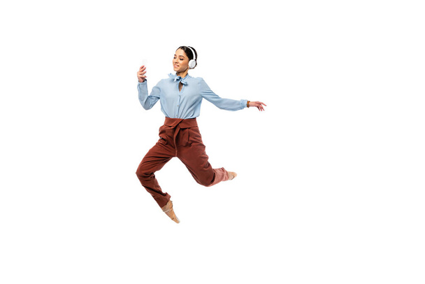 Smiling ballerina in headphones using smartphone while jumping isolated on white  - Foto, Imagen