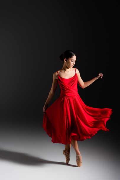 Young brunette ballerina in red dress dancing on black background  - Фото, зображення