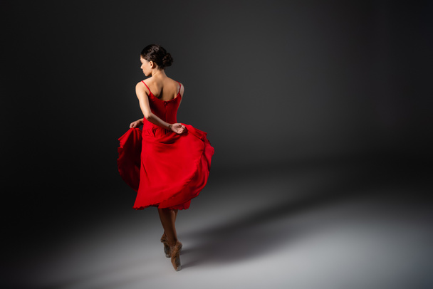 Side view of ballerina dancing and holding red dress on black background  - Foto, Imagem