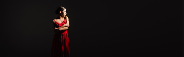 Πλευρική άποψη της όμορφης γυναίκας με κόκκινο φόρεμα στέκεται απομονωμένη σε μαύρο, banner  - Φωτογραφία, εικόνα