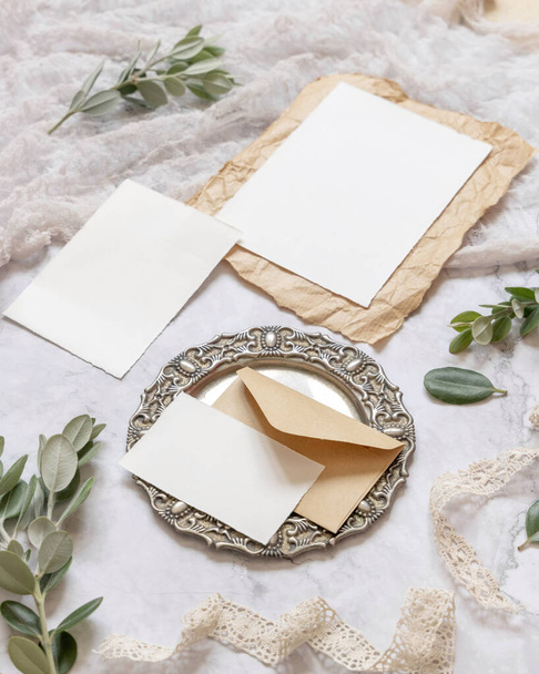 Bruiloft briefpapier set met envelop op een marmeren tafel versierd met eucalyptus takken en linten. Mock-up scene met blanco papieren wenskaarten. Vrouwelijke close-up - Foto, afbeelding