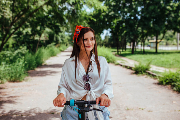 Menina morena bonito monta em uma scooter eletrodo no parque que ela está vestindo uma camisa branca. conceito de eco transporte e aluguel.  - Foto, Imagem