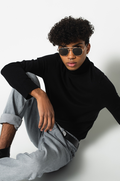 african american man in dark sunglasses and black turtleneck looking at camera while sitting on white - Photo, image