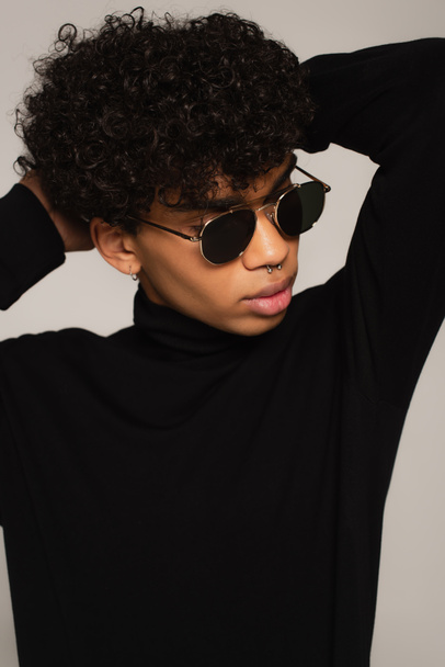 pierced african american man in black turtleneck and dark sunglasses posing with hands behind head isolated on grey - Fotoğraf, Görsel