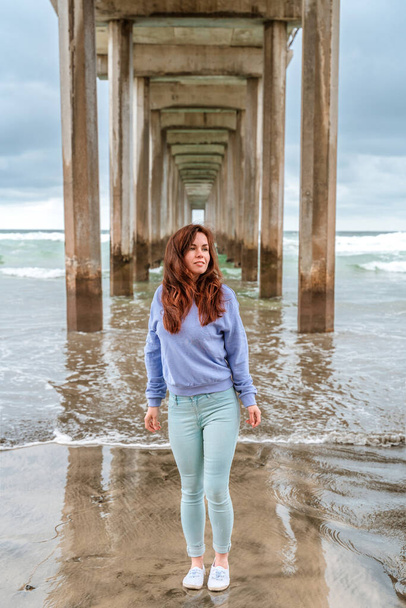 A beautiful young woman stands under La Jolla pier in cloudy weather. San Diego, California - Foto, Bild