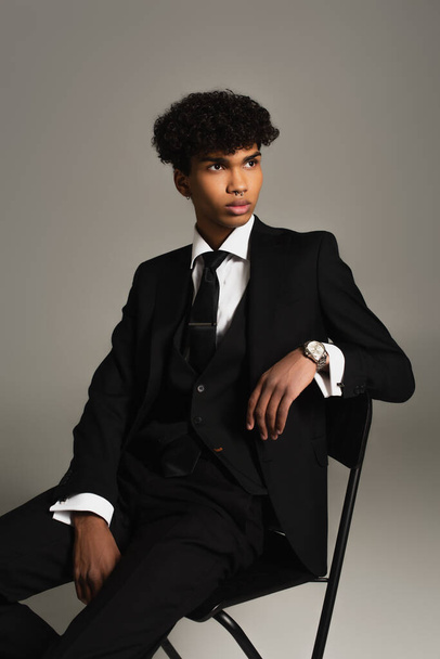 african american man in black three-piece suit sitting on chair and looking away isolated on grey - Foto, immagini