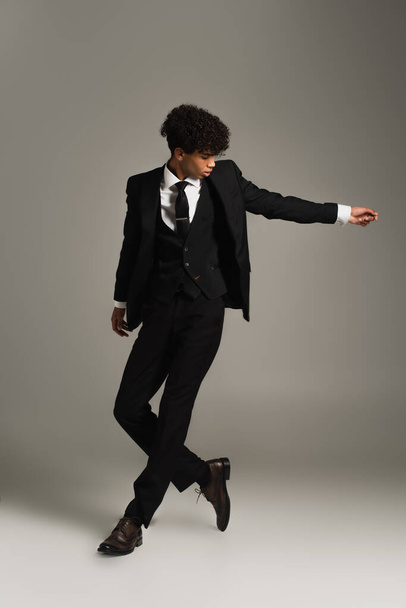 full length view of african american man posing in elegant three-piece suit and oxford shoes on grey - Foto, imagen