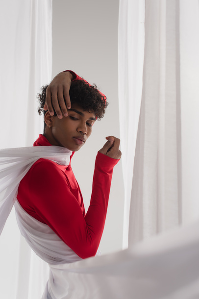 stylish african american man posing in red turtleneck near white drapery - Photo, Image