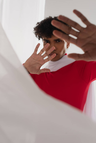 fiatal afro-amerikai férfi piros garbó mutatja stop gesztus közelében fehér elmosódott ruha - Fotó, kép
