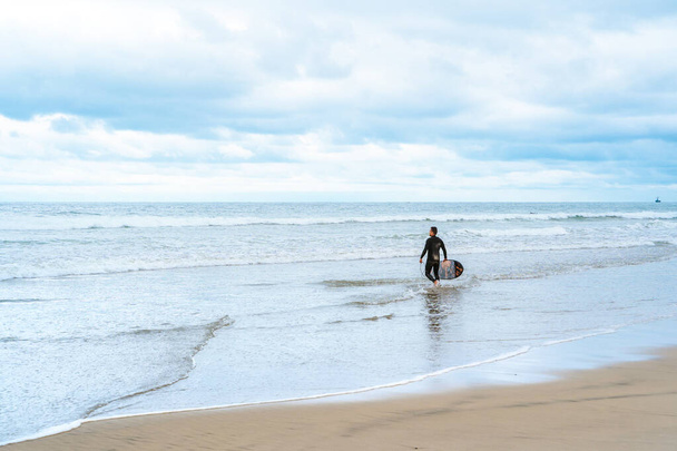 Surffaaja laudalla kävelee pitkin merta Kaliforniassa pilvisenä päivänä. San Diego, Yhdysvallat - 22 huhti 2021 - Valokuva, kuva