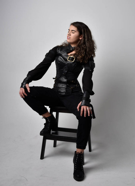 Full length portrait of young woman with natural brown hair,  wearing black leather scifi outfit with corset, standing pose on light grey studio background. - Foto, afbeelding