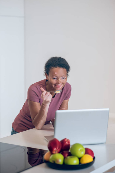 Dark-skinned young woman having breakfast at home and watching somethig on a laptop - Фото, зображення