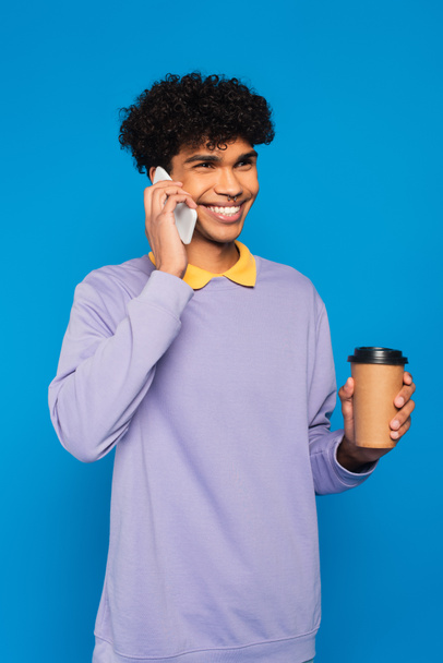 cheerful african american man with takeaway drink talking on mobile phone isolated on blue - Photo, Image