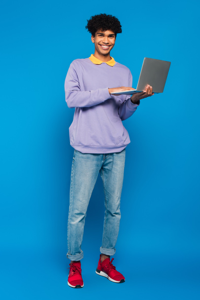 teljes hosszúságú nézet afro-amerikai diák segítségével laptop kék háttér - Fotó, kép